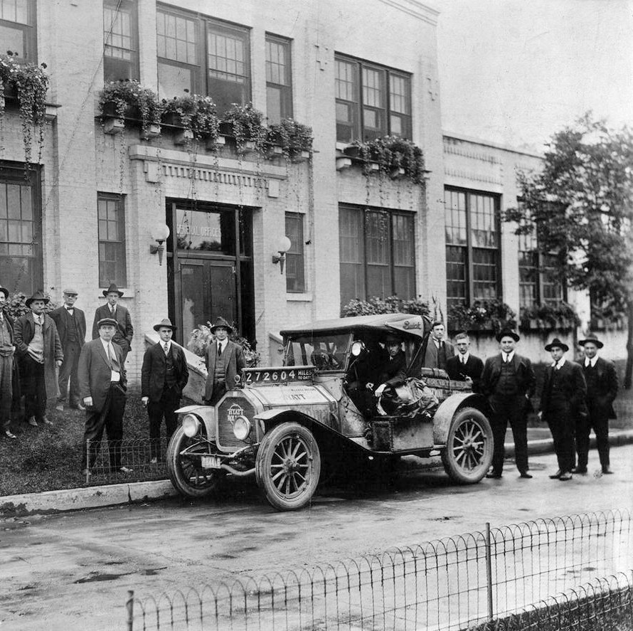 Historic photograph of a group of men and an early automobile outside a Clark Equipment building